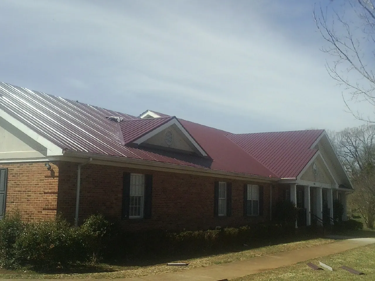 Red metal roof with gabled entries on a long brick building, from a Hail Damage Roof Repair job in Cowiche