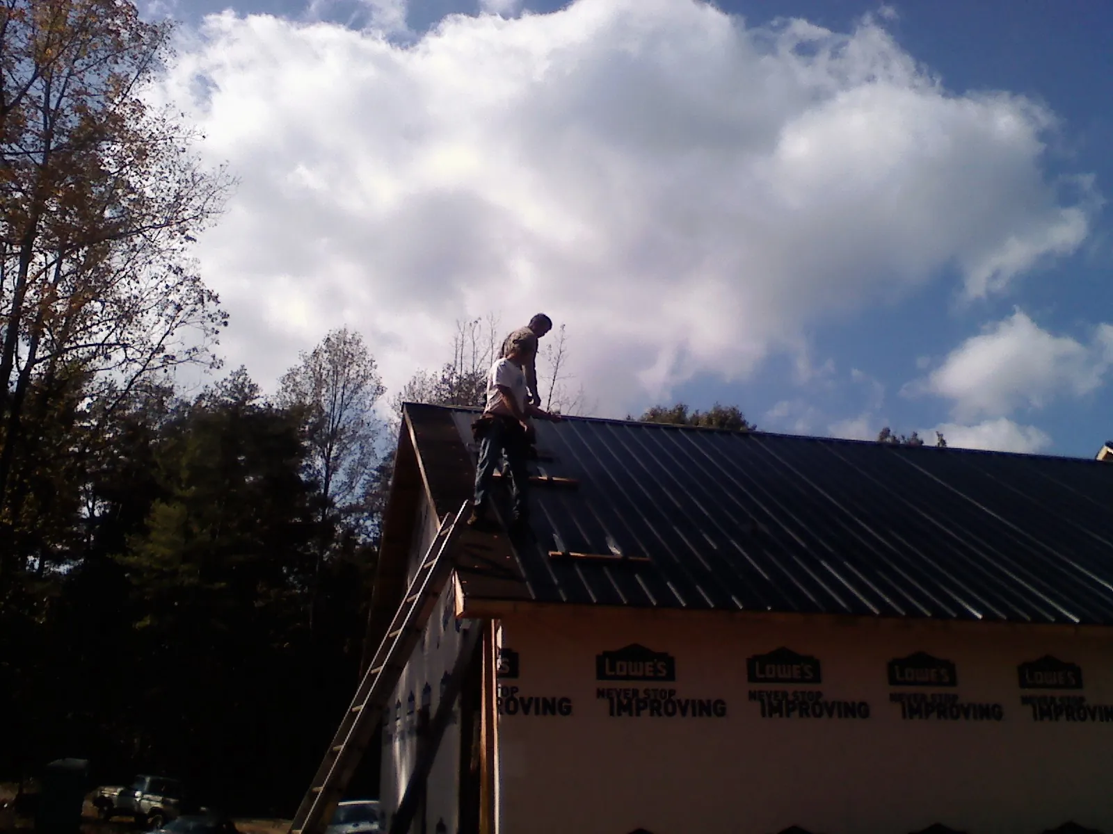 Roofer fastening dark metal panels high against a cloudy sky, from a Roof Inspection job in Cowiche