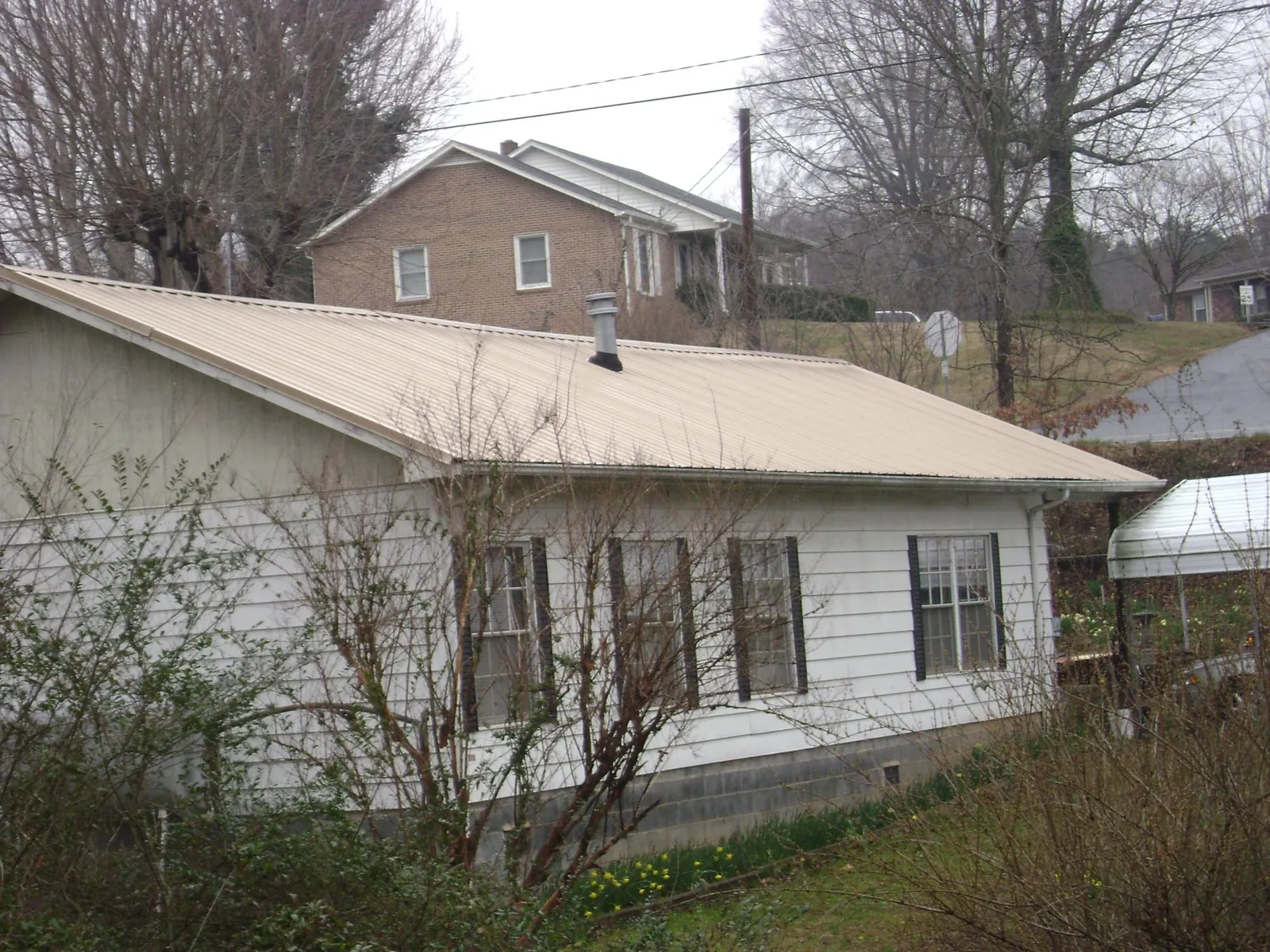 Tan metal roof on a white sided house set into a hillside — Commercial Roofing by Roofing Brothers in Cowiche